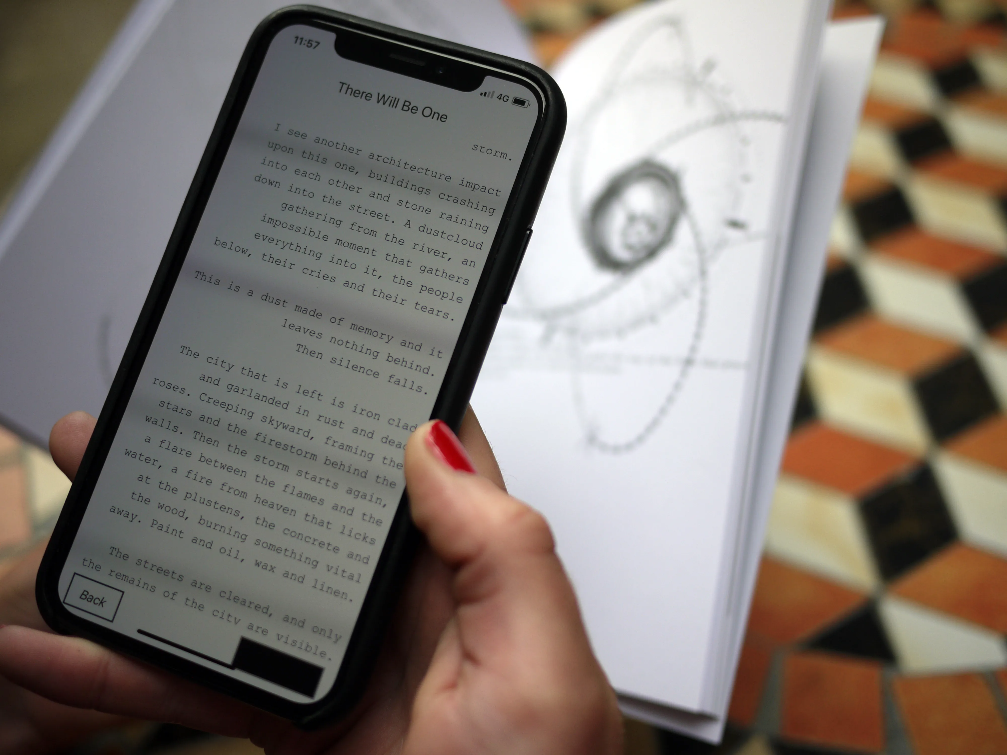 A hand holds a phone showing prose text from These Pages Fall Like Ash, beside a printed book on a tiled floor
